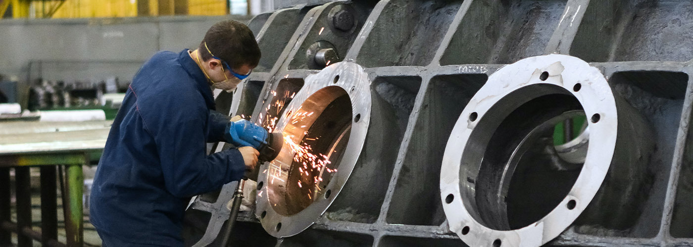 manufacturing employee using a grinder on a large piece of metal